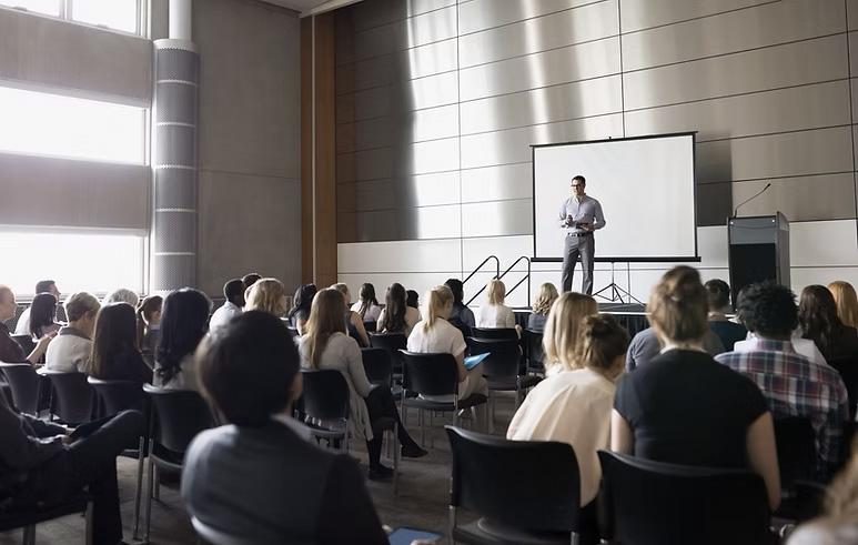 Conférencier devant public dans une salle de conférence.